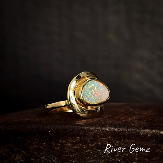 Gold ring with an opal stone on a dark background, featuring the brand 'River Gemz'.