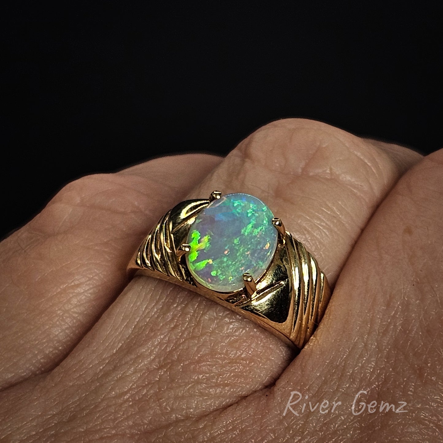 Gold ring with a light opal on a hand, branded 'River Gemz'.