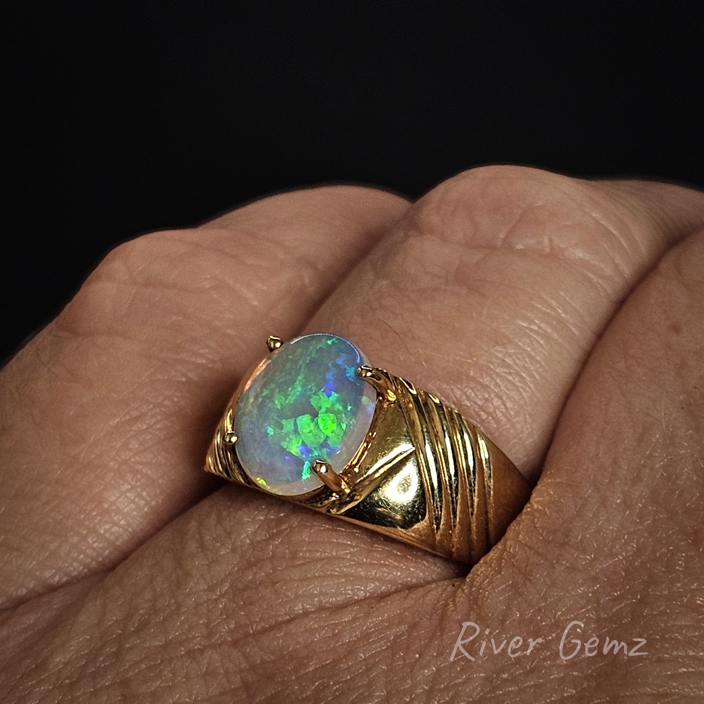 Gold ring with an opal stone on a hand, branded 'River Gemz'.