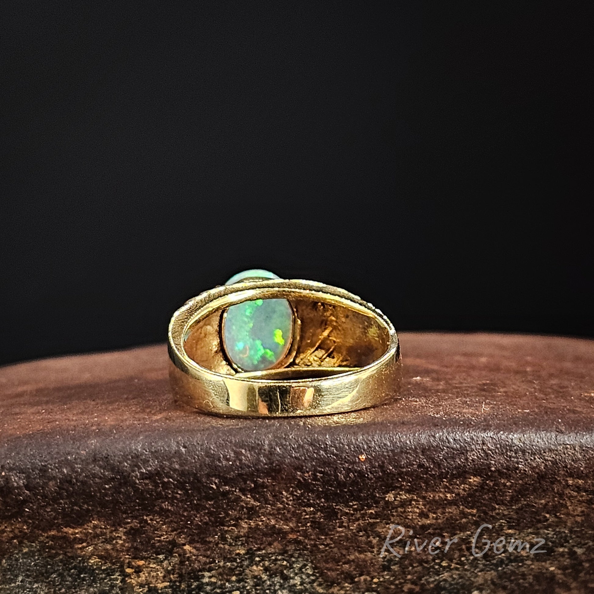 Rear view of the gold ring showing the light base tone of the crystal opal set within it on a dark background
