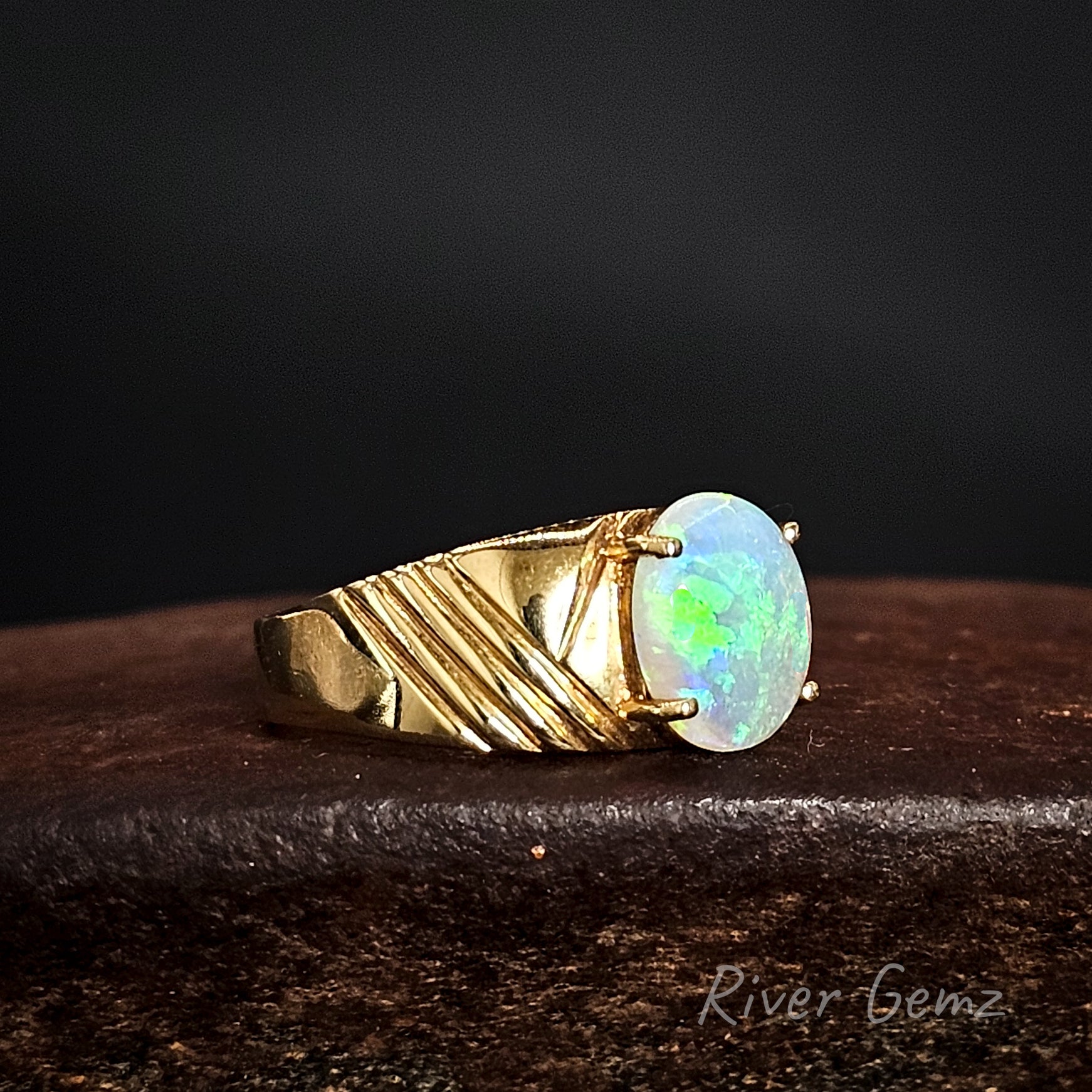 Gold ring with an oval shaped green crystal opal on a dark background