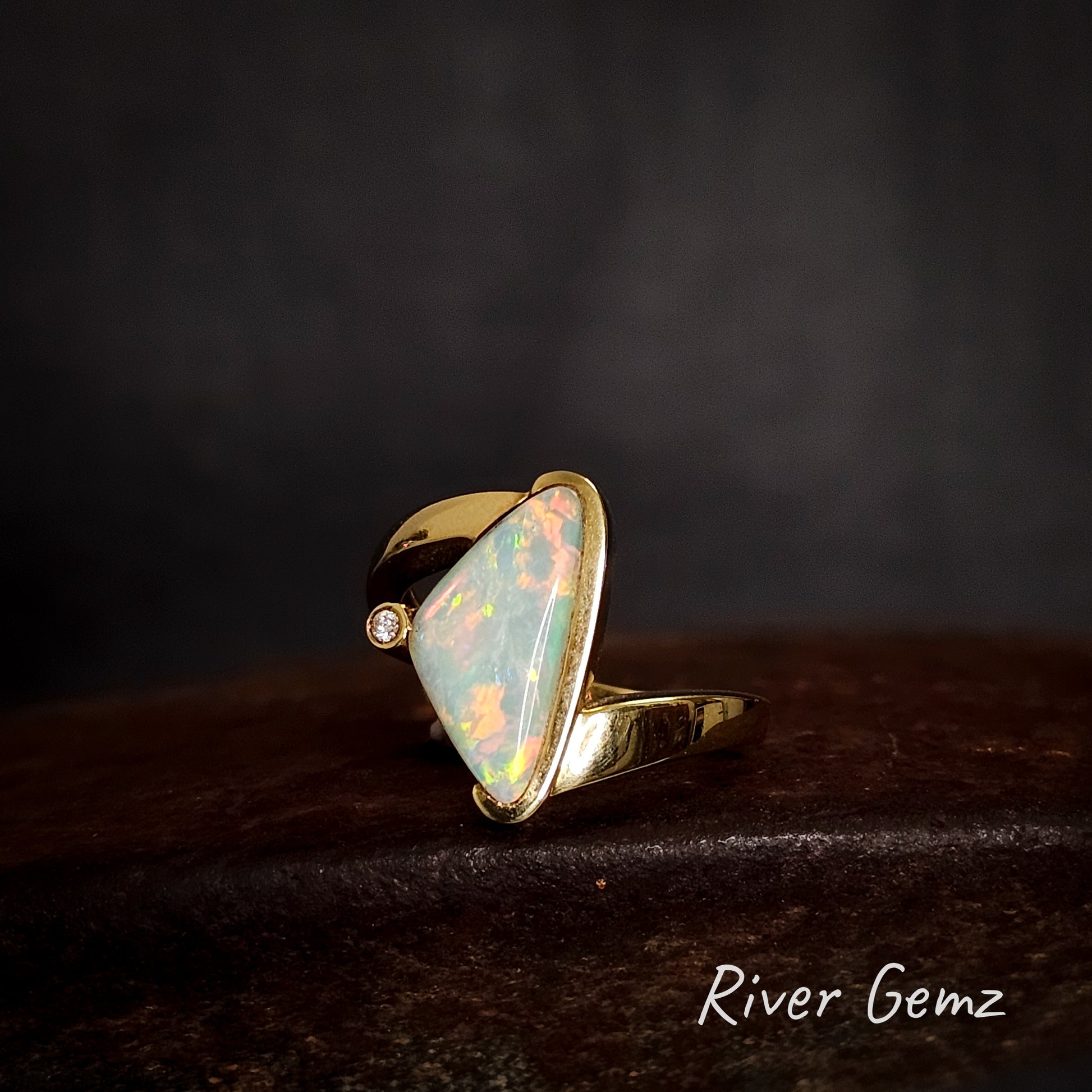 Opal and diamond ring with gold setting on a dark background, branded 'River Gemz'.
