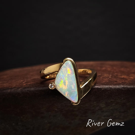 Gold ring with a triangular crystal opal stone and diamond on a dark background, branded 'River Gemz'.