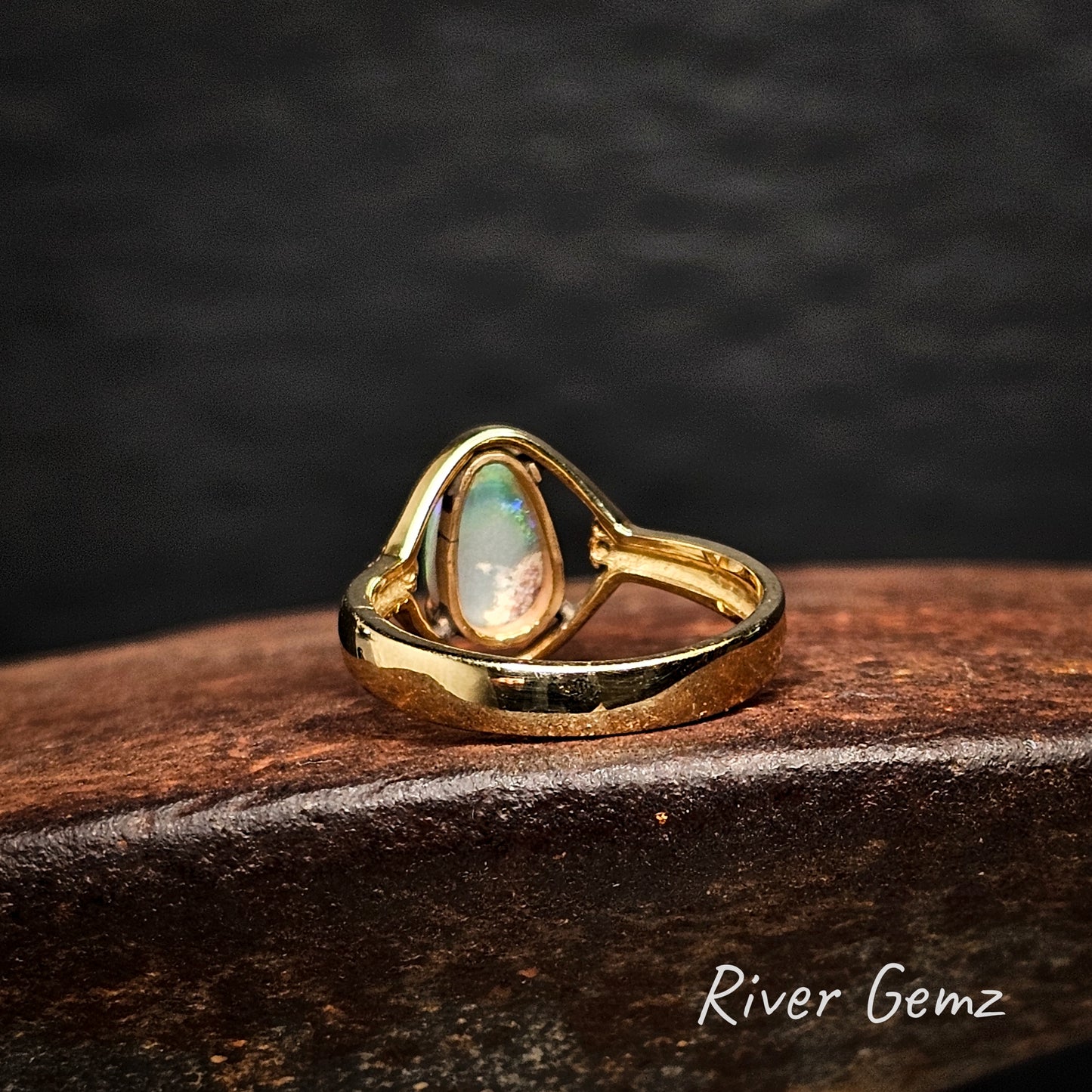 Rear view of gold ring with an opal stone on a cast iron shoe anvil, branded 'River Gemz'.