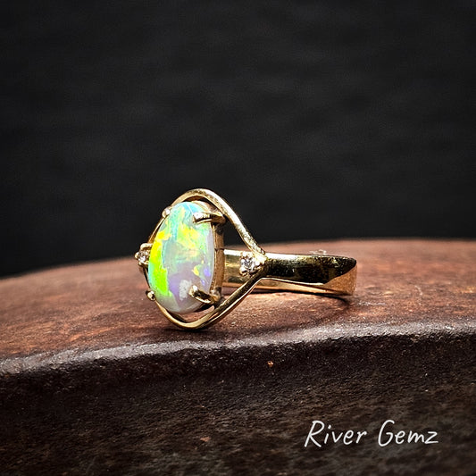 Gold ring with an opal stone on a dark background, branded 'River Gemz'.