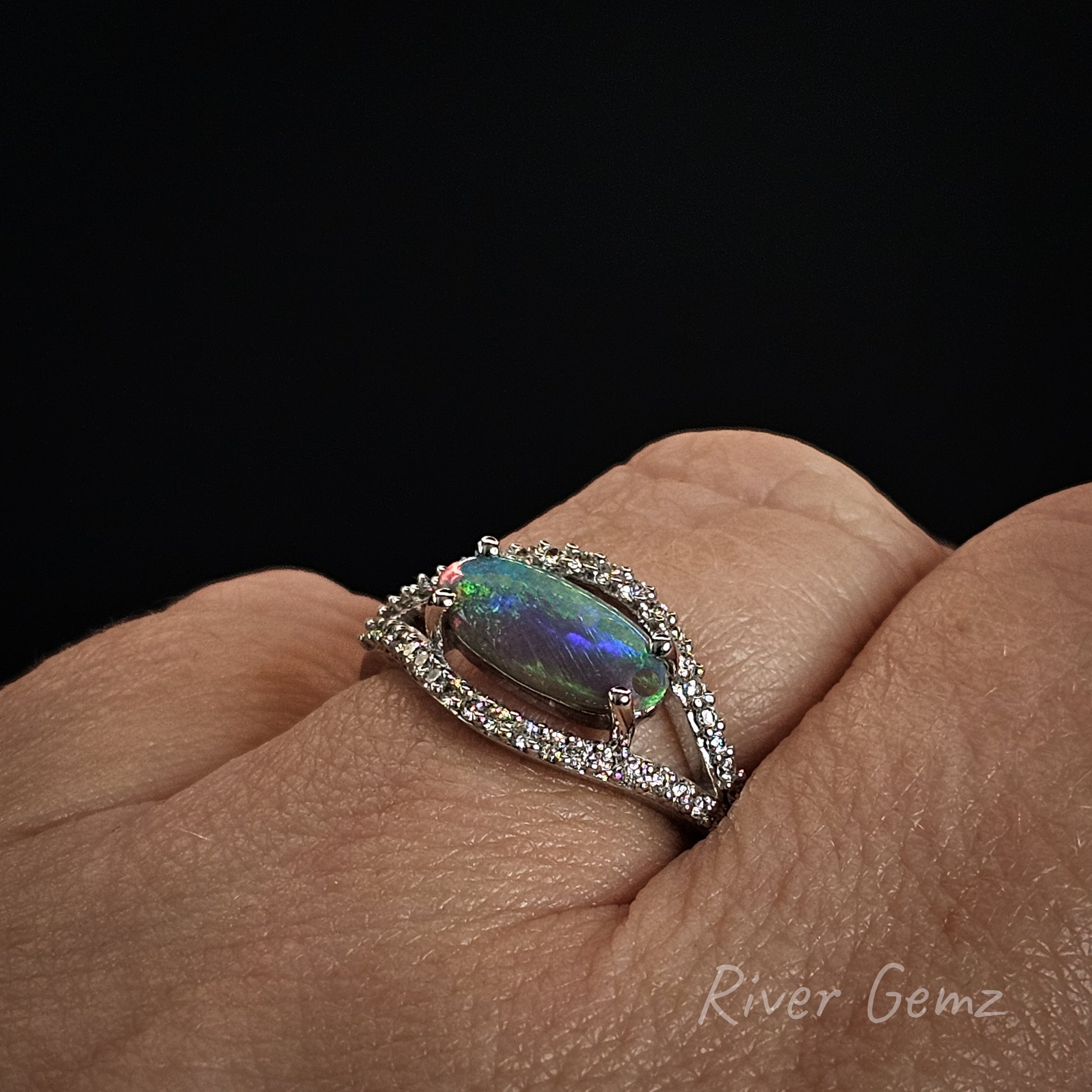 Ring with a colorful gemstone on a finger against a black background
