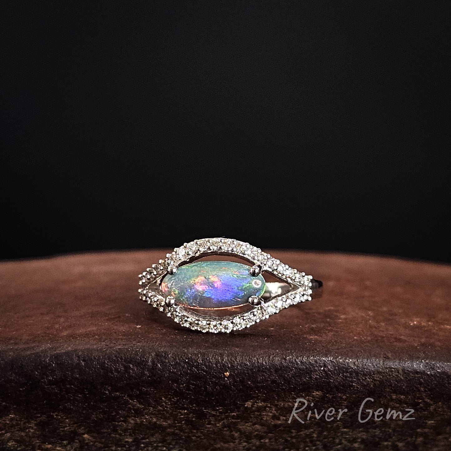 Opal ring with diamond accents on a dark background, branded 'River Gemz'.