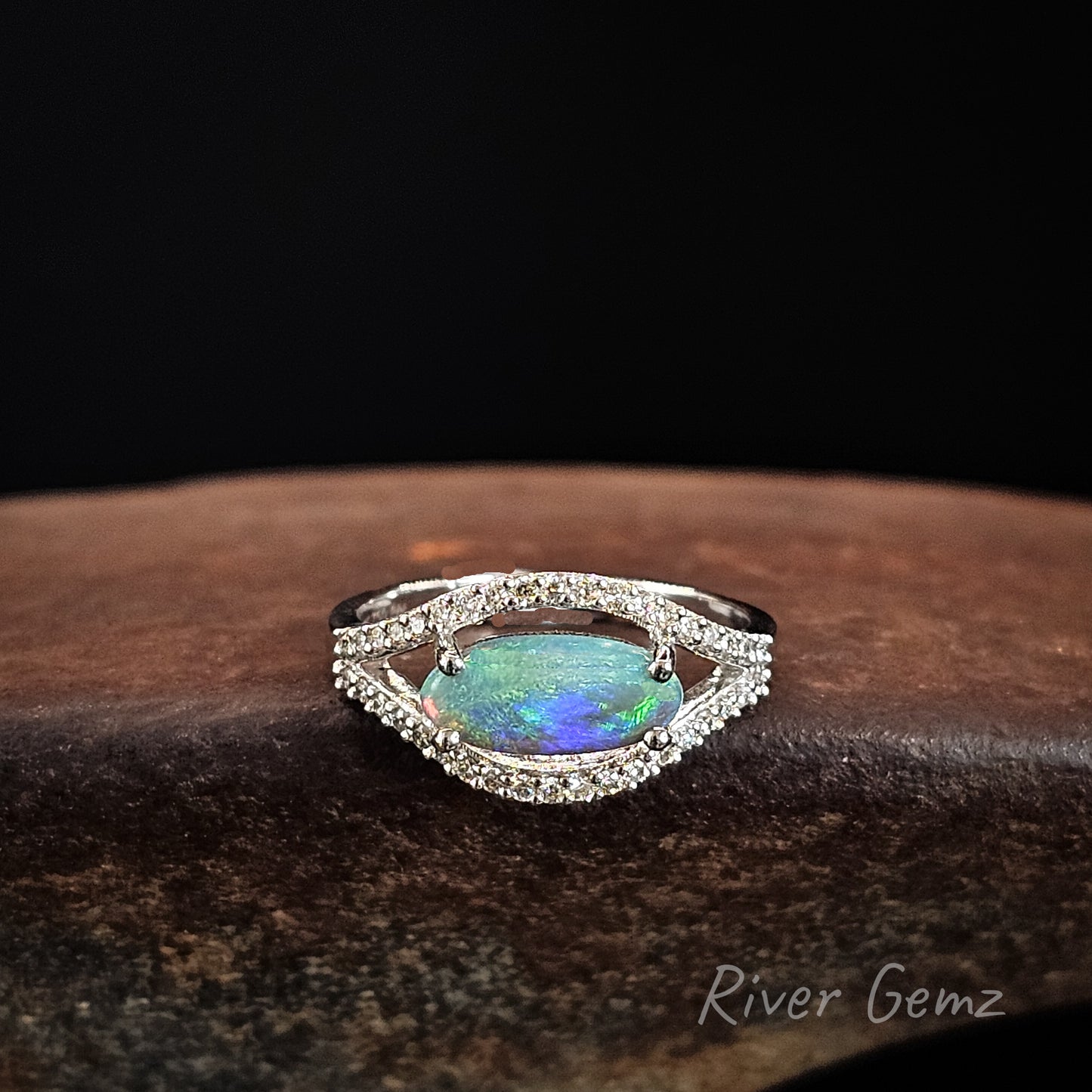 Opal ring with diamond accents on a dark surface, branded 'River Gemz'.