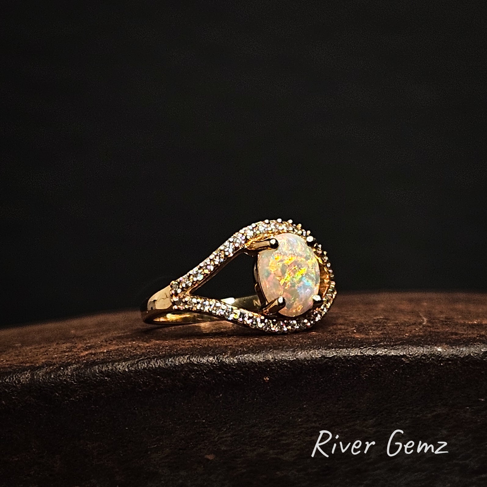 Opal ring with gold and diamond accents on a dark background, branded 'River Gemz'.