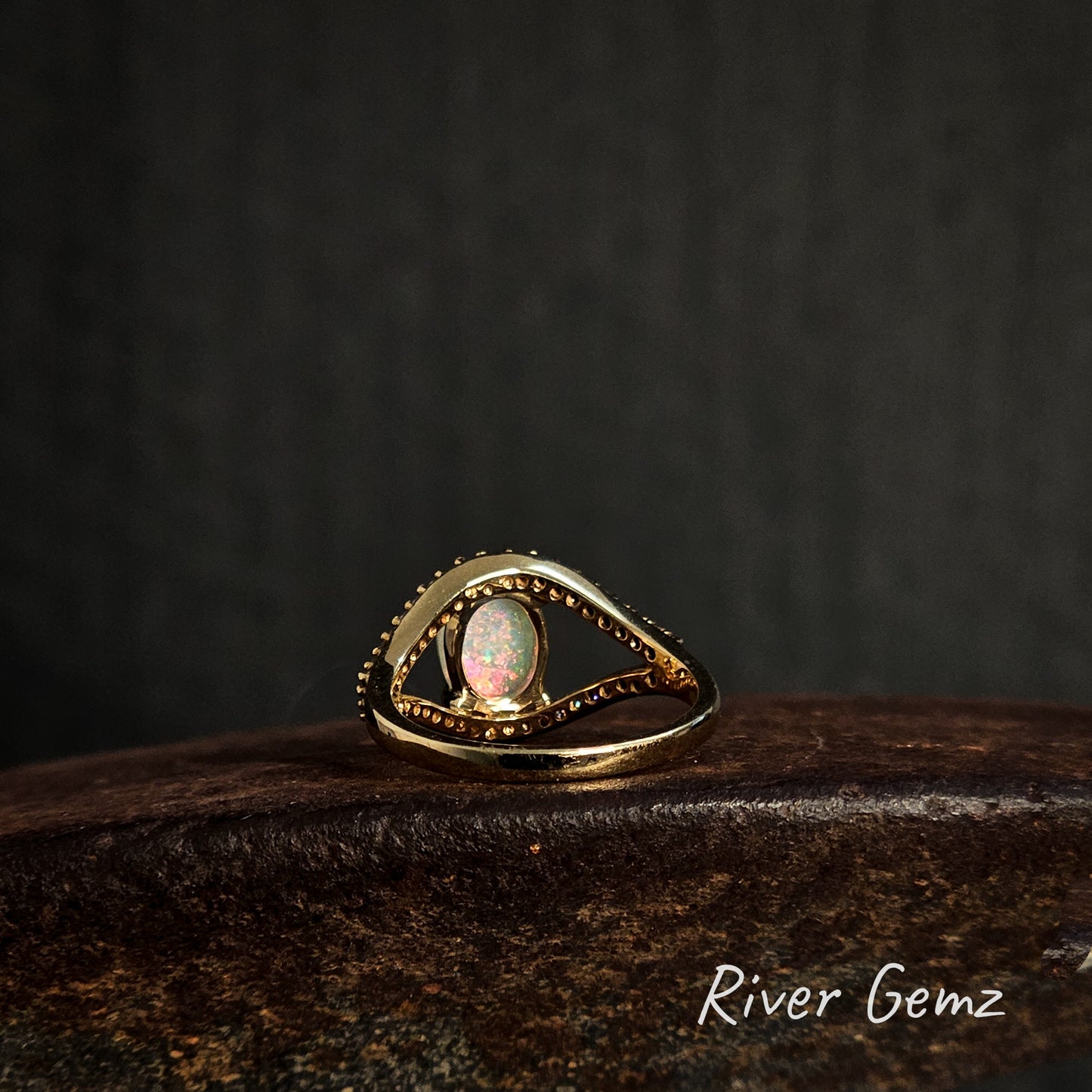 Rear view of the gold ring with an opal stone on a dark background, featuring the brand 'River Gemz'.