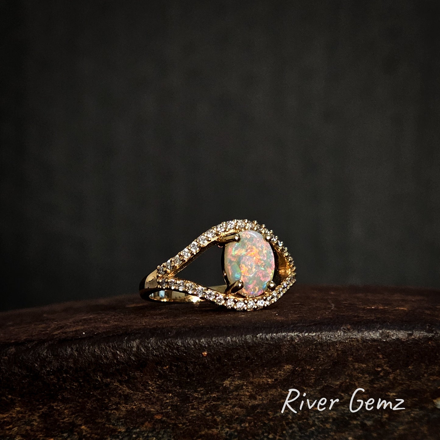 Opal ring with gold and diamond accents on a dark background, featuring the brand 'River Gemz'.