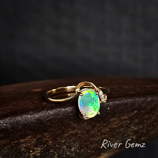 Gold ring with a claw set bright green light opal on a dark surface, branded 'River Gemz'.