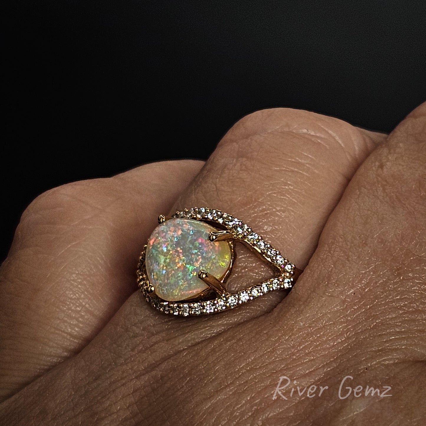 Ring with a colorful gemstone on a finger, branded 'River Gemz'.