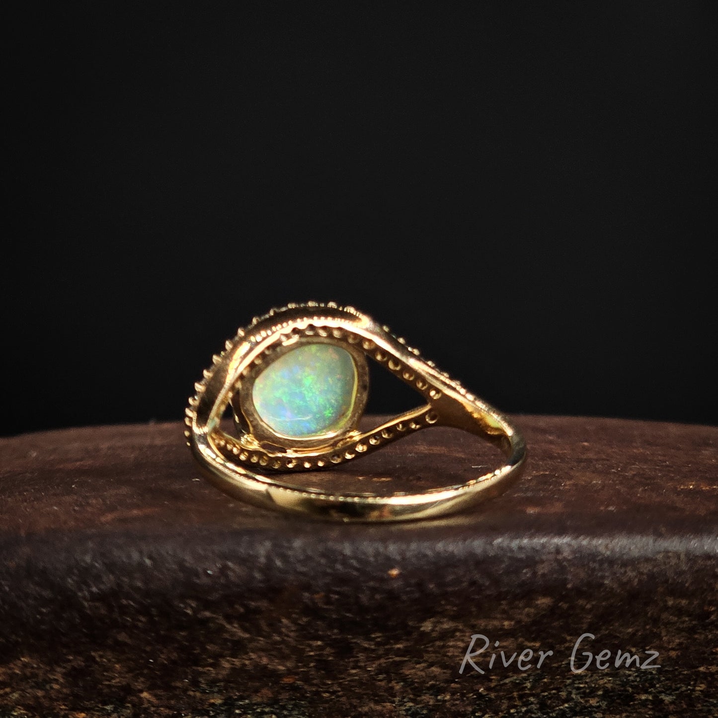 Rear view of the gold ring showing the light base tone of the crystal opal on a dark background, branded 'River Gemz'.