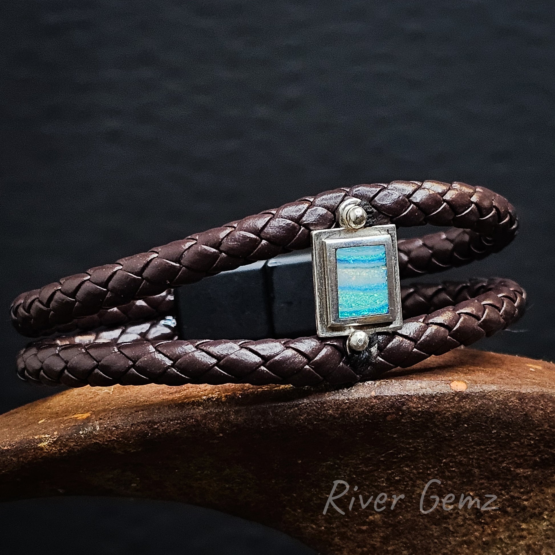 Soft-coloured rectangular shaped opal besel set in sterling silver and attached to a brown braided leather bracelet.