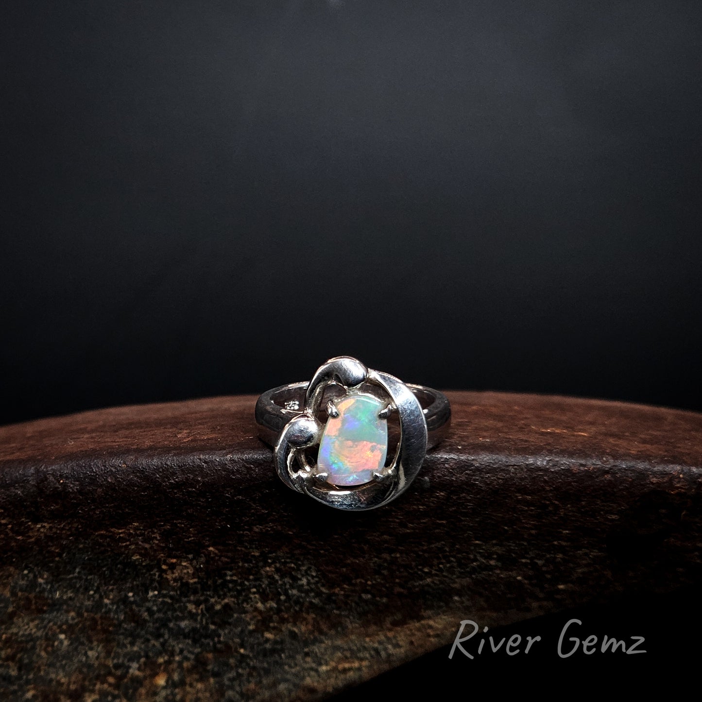 Oranges interspersed with greens in a free-form cut crystal opal set in a floral type silver ring design.