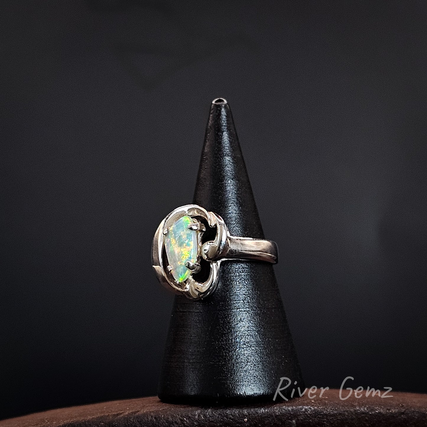 A sterling silver ring with a round iridescent opal gemstone, displayed on a black cone stand against a dark background.