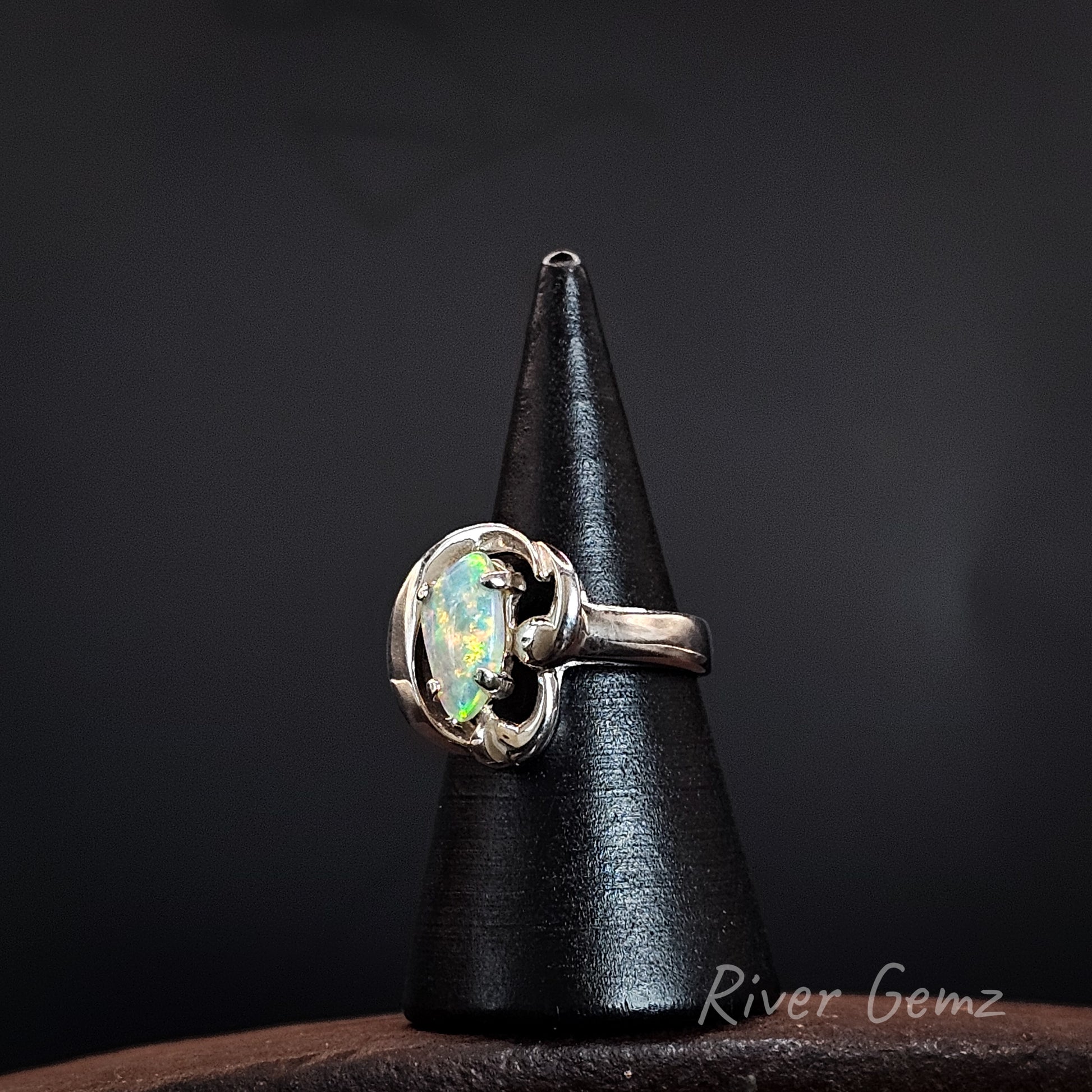 A sterling silver ring with a round iridescent opal gemstone, displayed on a black cone stand against a dark background.