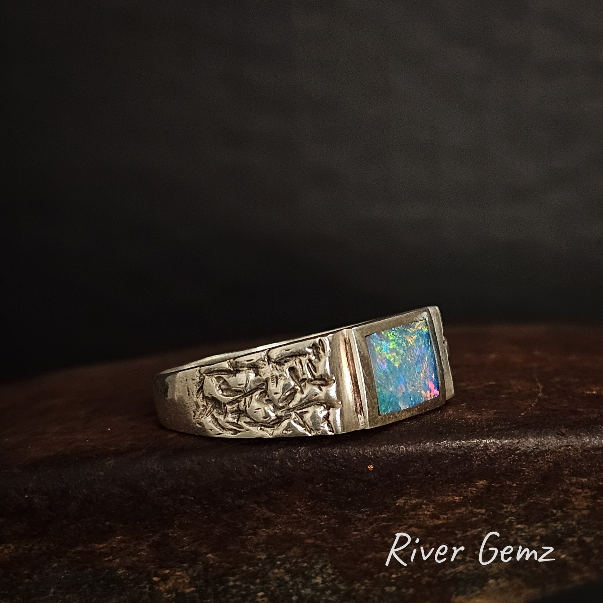 Side view of silver ring with rectangular shaped opal stone on a dark background, featuring 'River Gemz' branding.