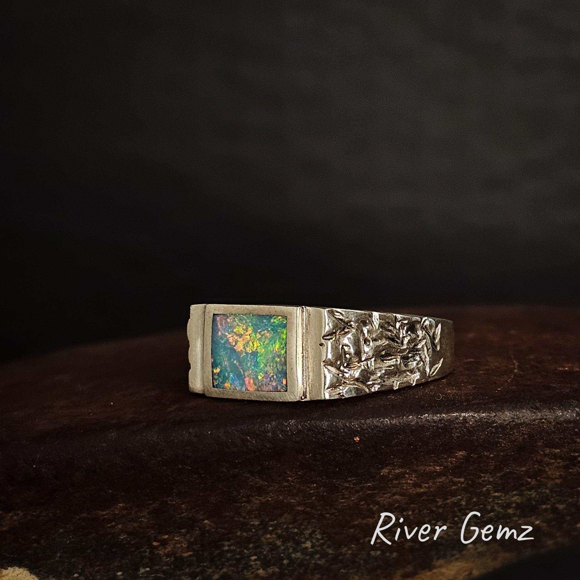 Silver ring with colorful crystal opal and pummeled silver shoulders on a dark background, branded 'River Gemz'.