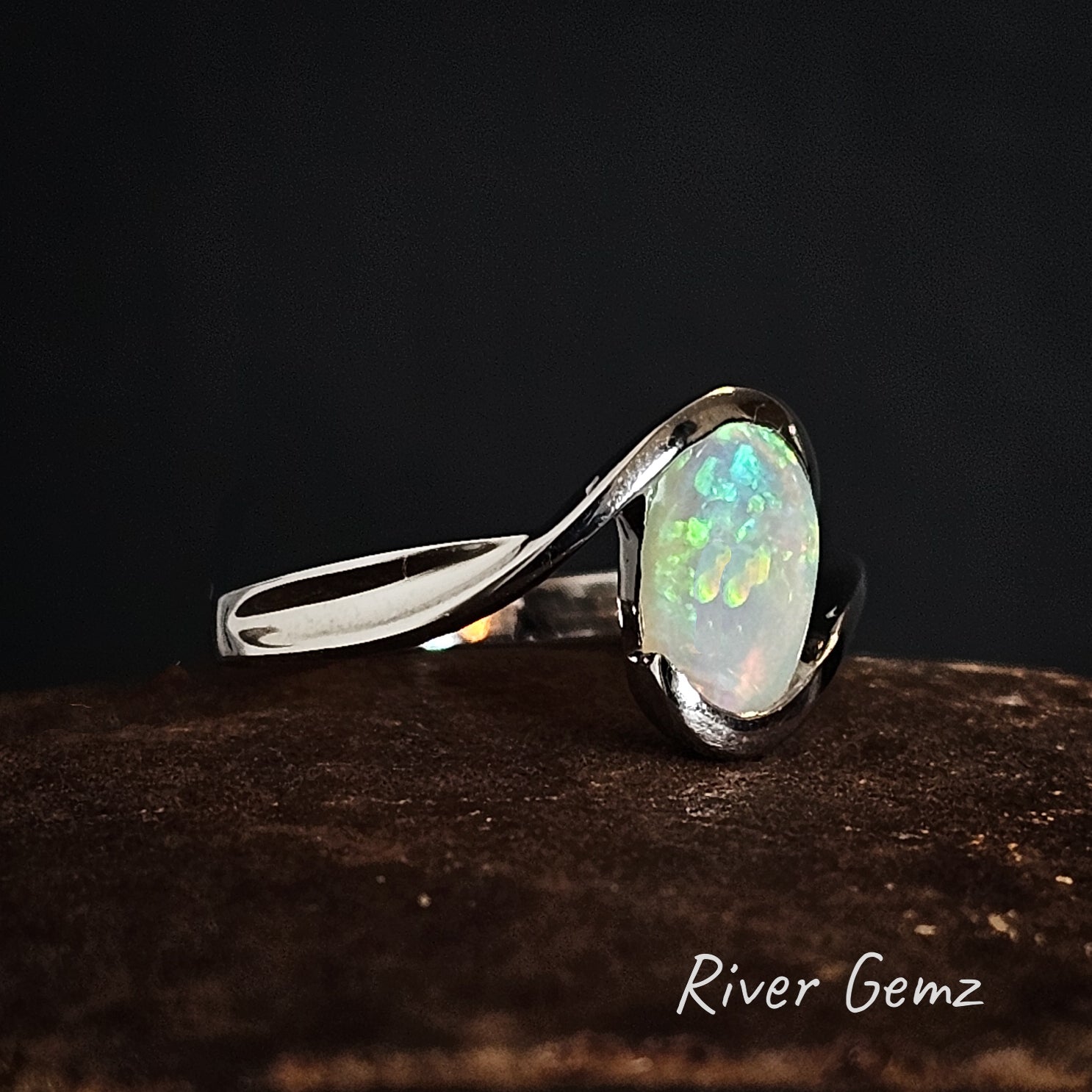 Silver ring with a light opal stone on a dark background, branded 'River Gemz'.