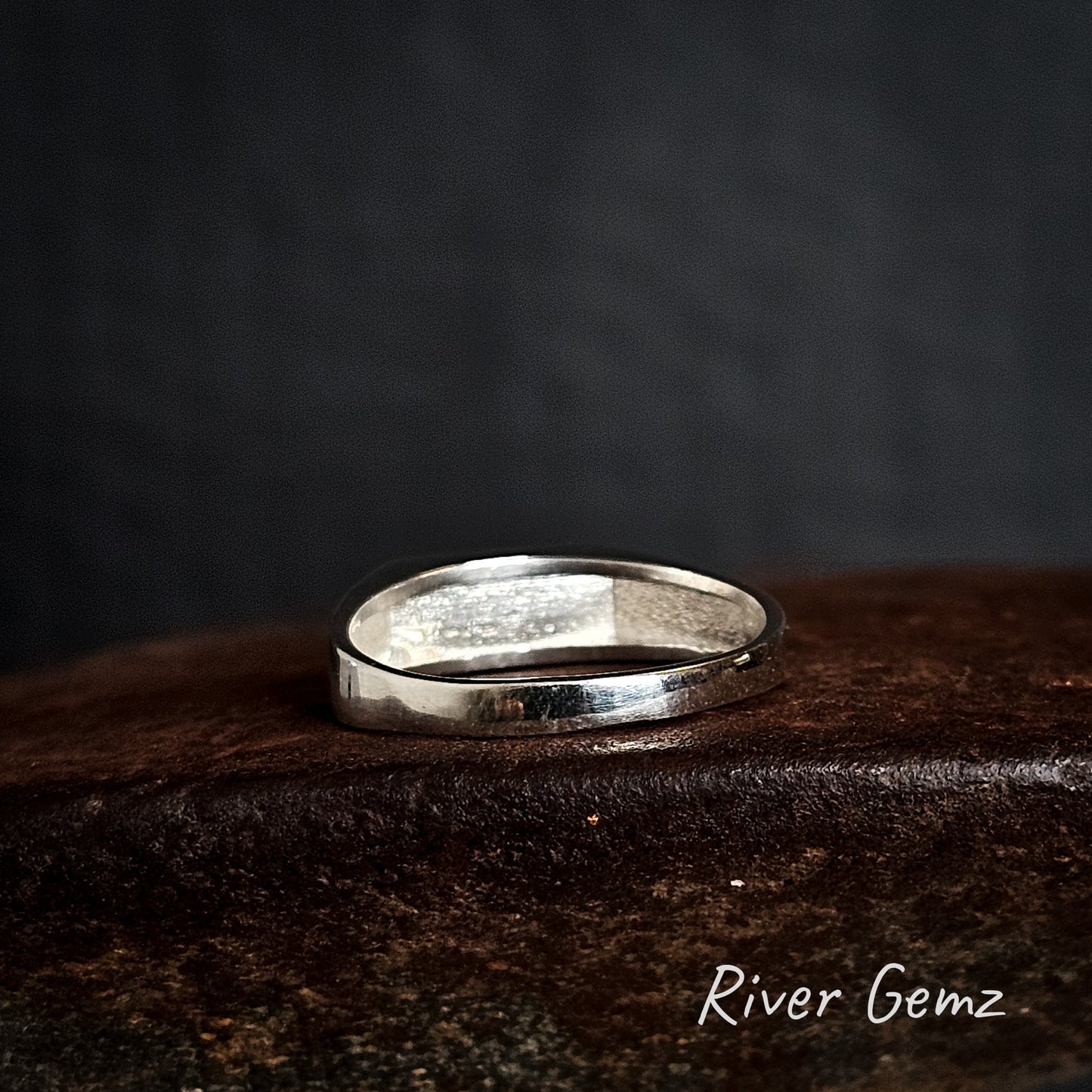 Rear view of silver ring on a dark textured surface with 'River Gemz' branding.