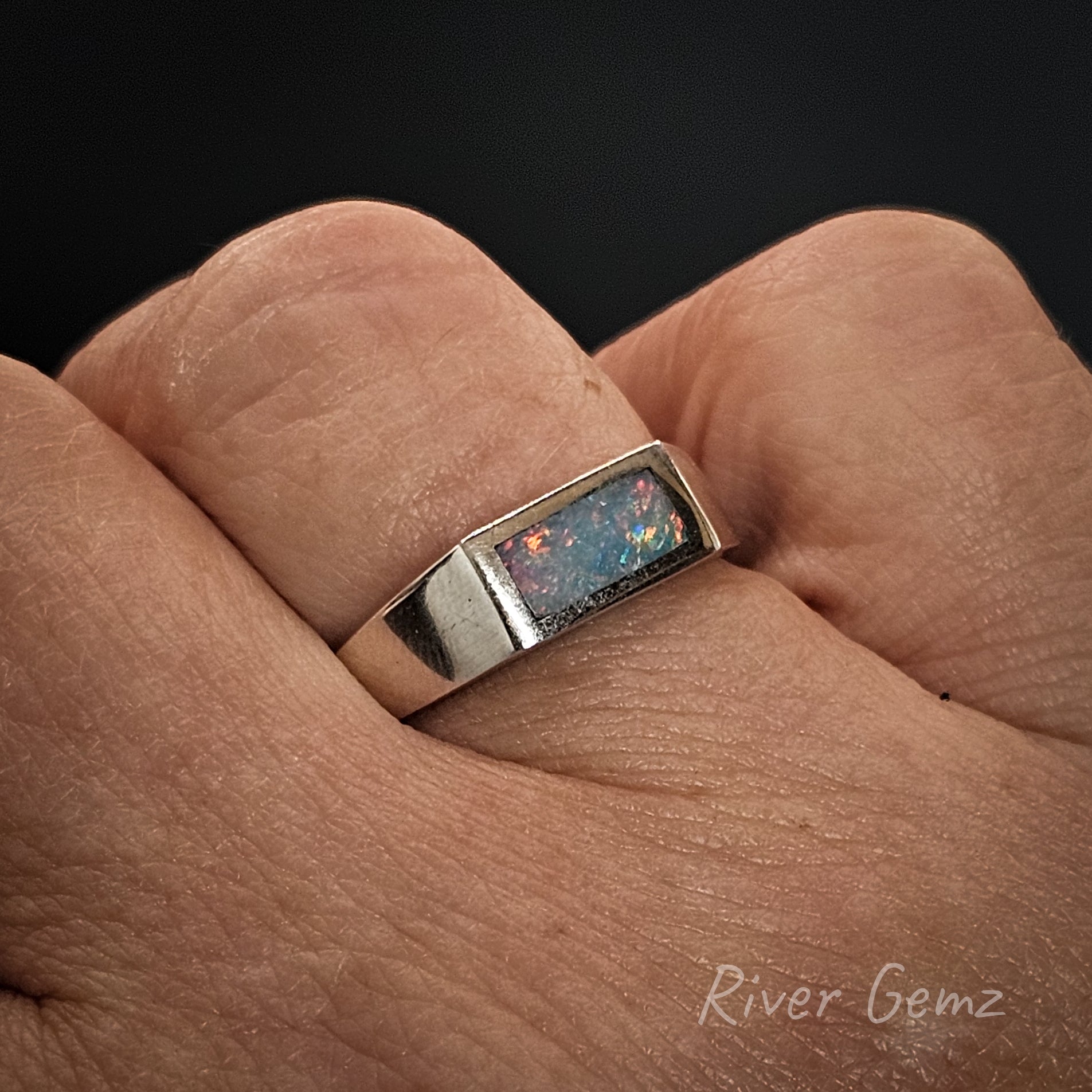 Ring with opal stone on a finger, brand 'River Gemz' visible