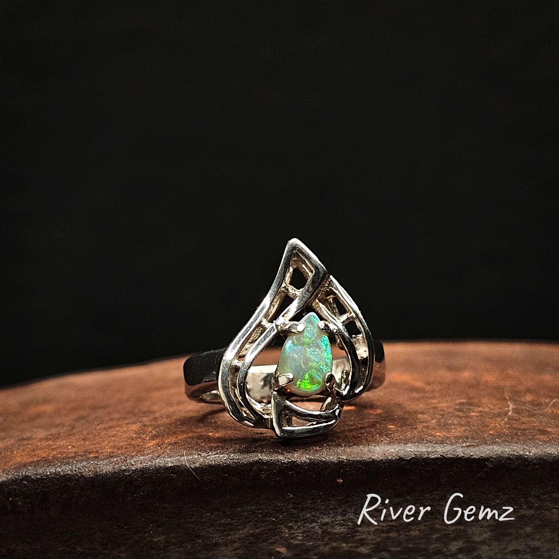 Silver ring with a green gemstone on a dark background, branded 'River Gemz'.