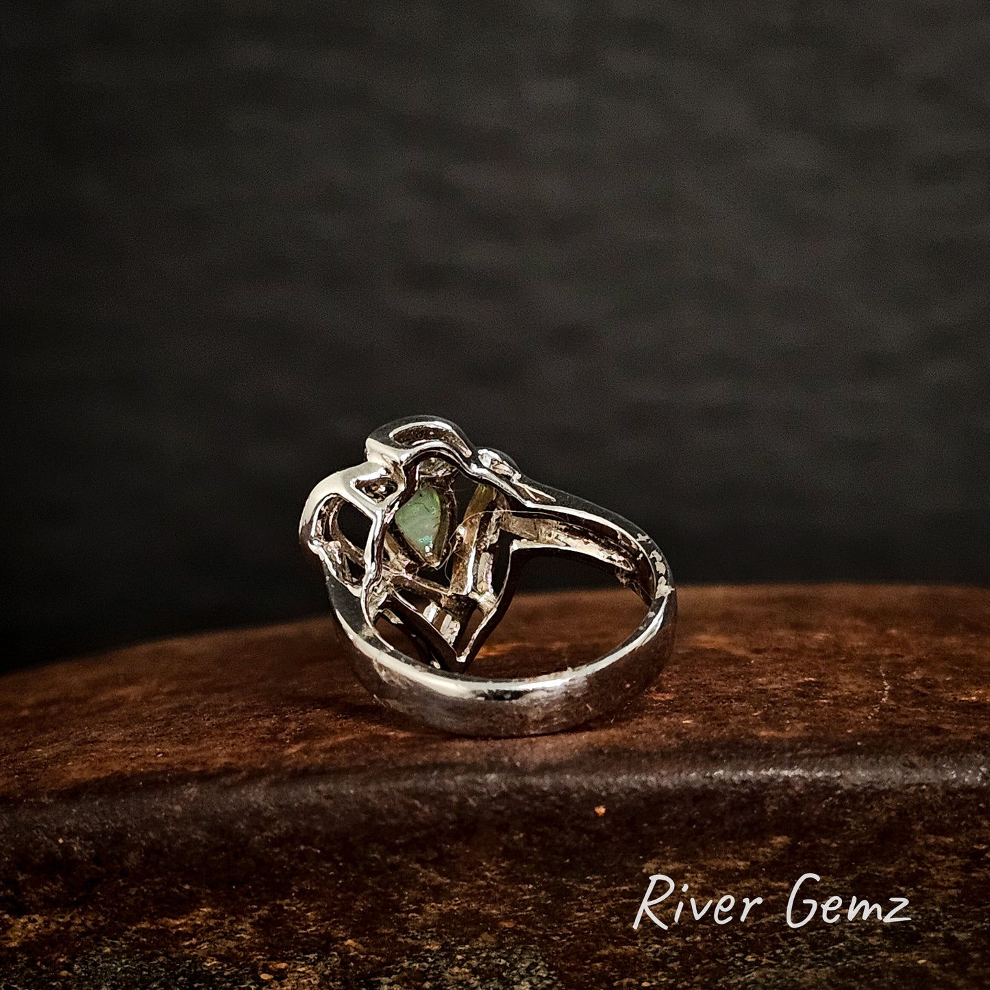 Back of silver ring shows the light base tone of the crystal opal on a dark wooden surface, branded 'River Gemz'.