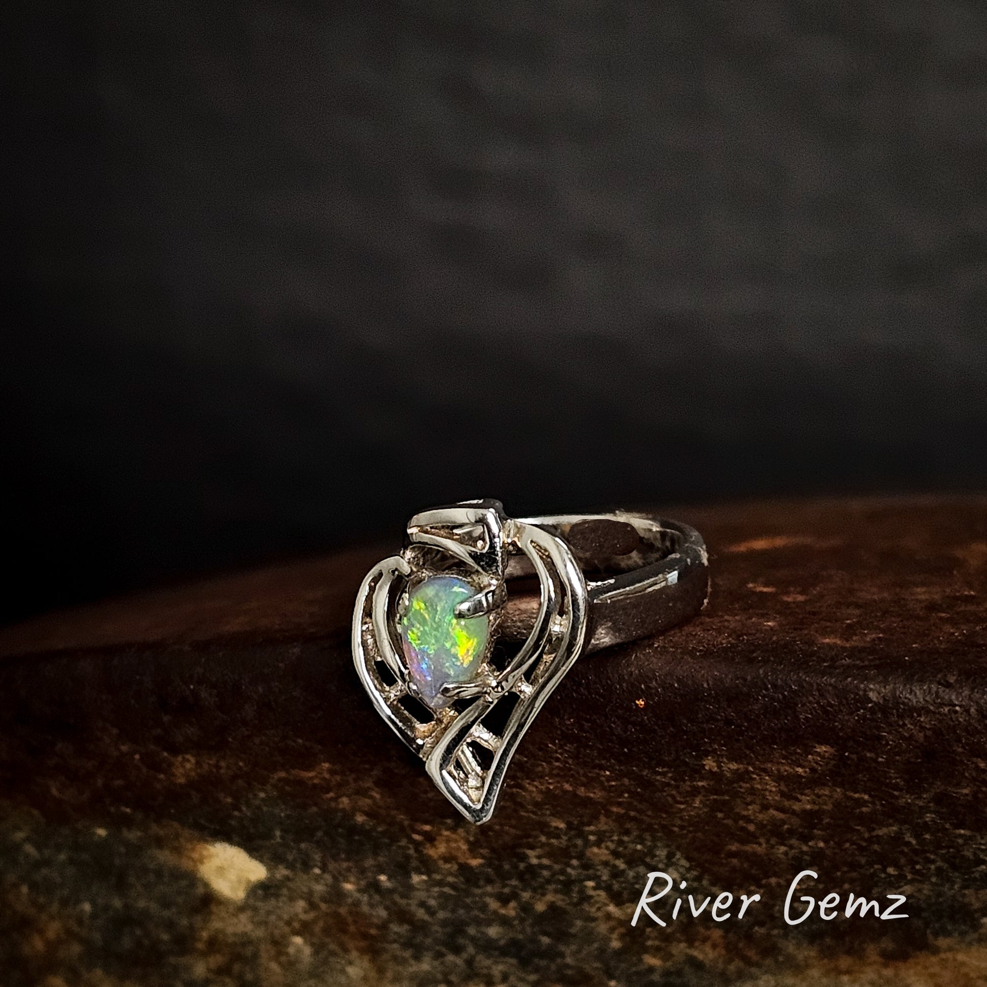 Silver ring with a tear-drop shaped blue and green opal stone on a dark background, branded 'River Gemz'.