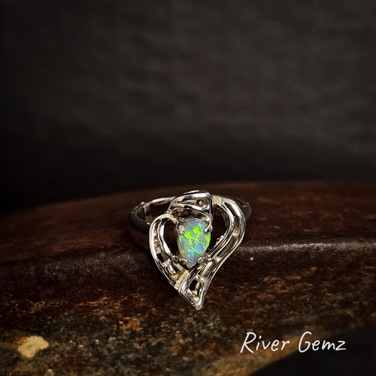 Heart-shaped silver ring with a claw set opal stone on a dark background, branded 'River Gemz'.