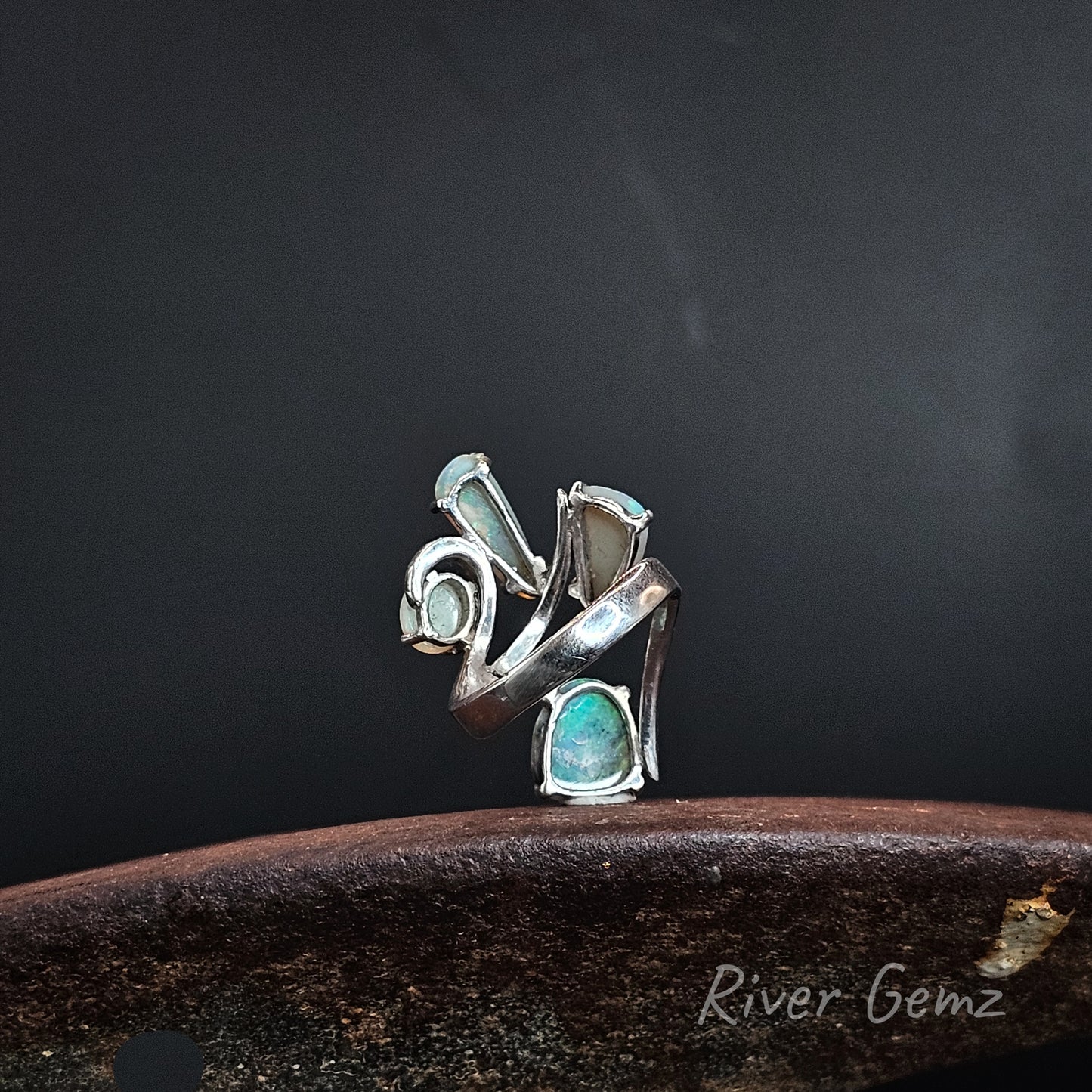 Rear view of a silver ring showing the light base tone of the 4 crystal opals set in it. The brand name 'River Gemz' is visible in the bottom right corner.