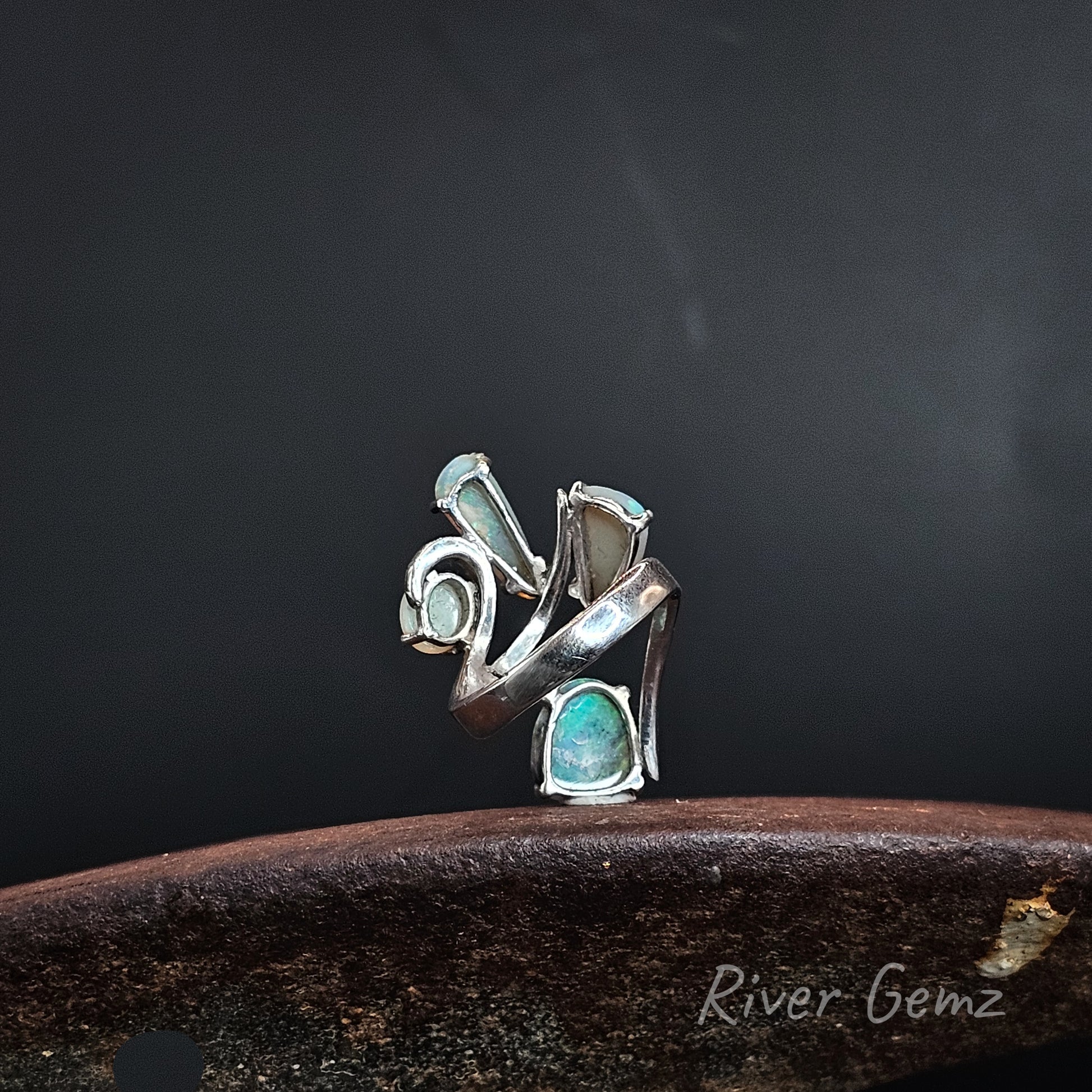 Rear view of a silver ring showing the light base tone of the 4 crystal opals set in it. The brand name 'River Gemz' is visible in the bottom right corner.