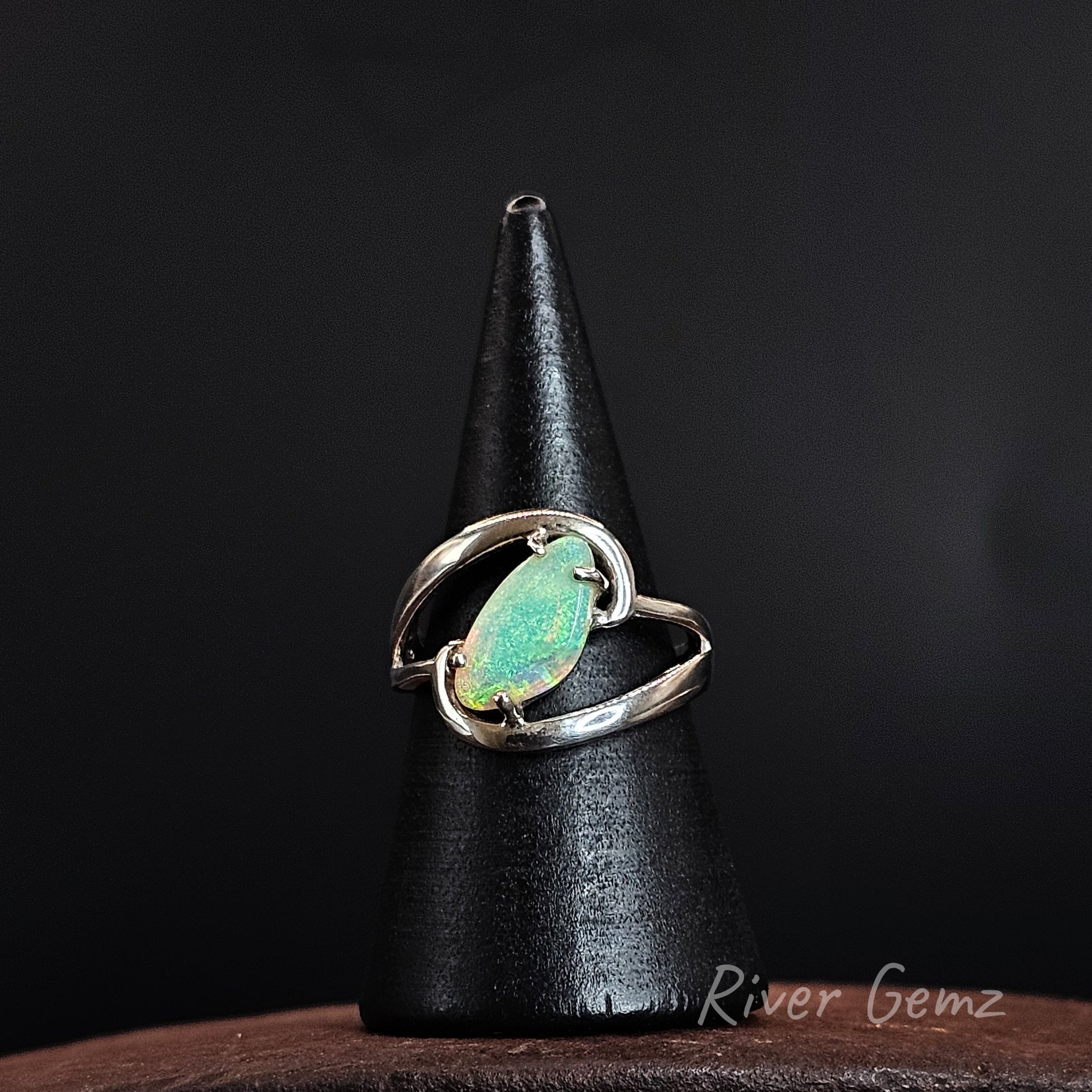 A sterling silver ring with a marquise-cut green opal gemstone, displayed on a black cone stand against a dark background.
