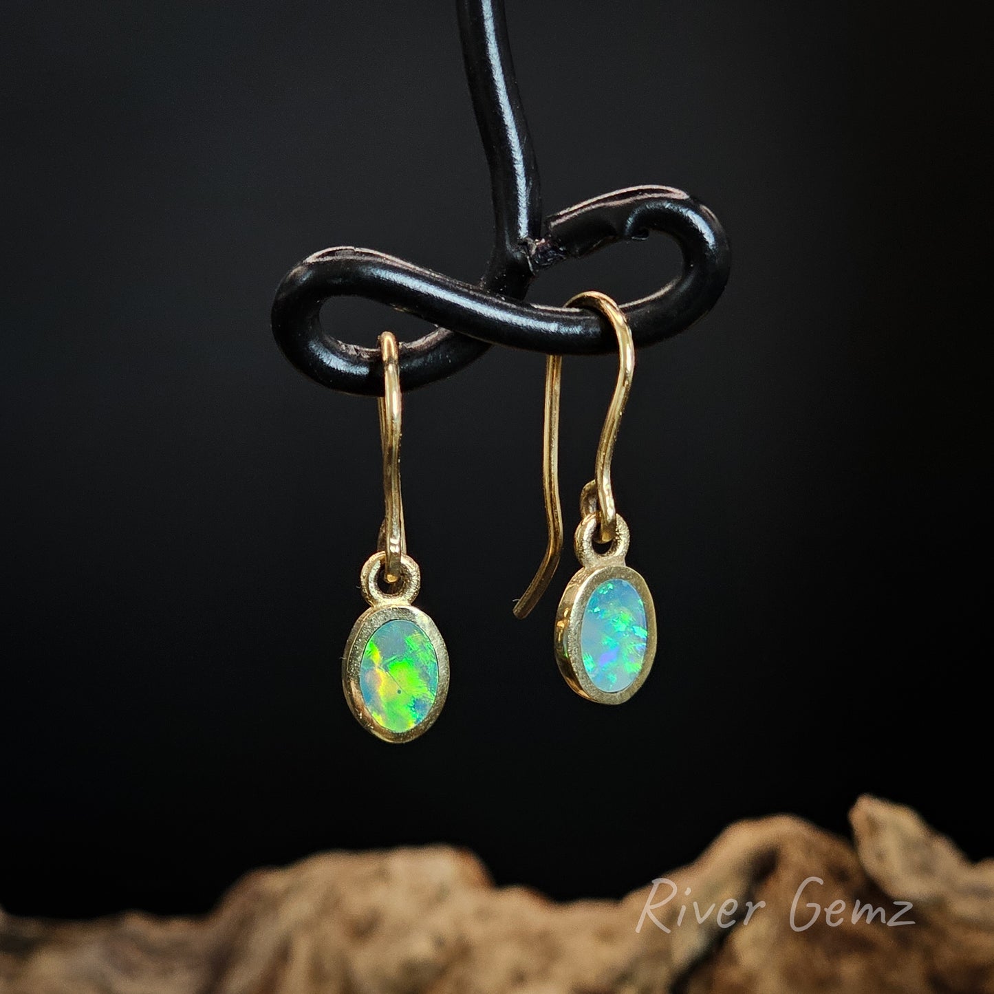 Opal earrings on a black stand with a dark background.