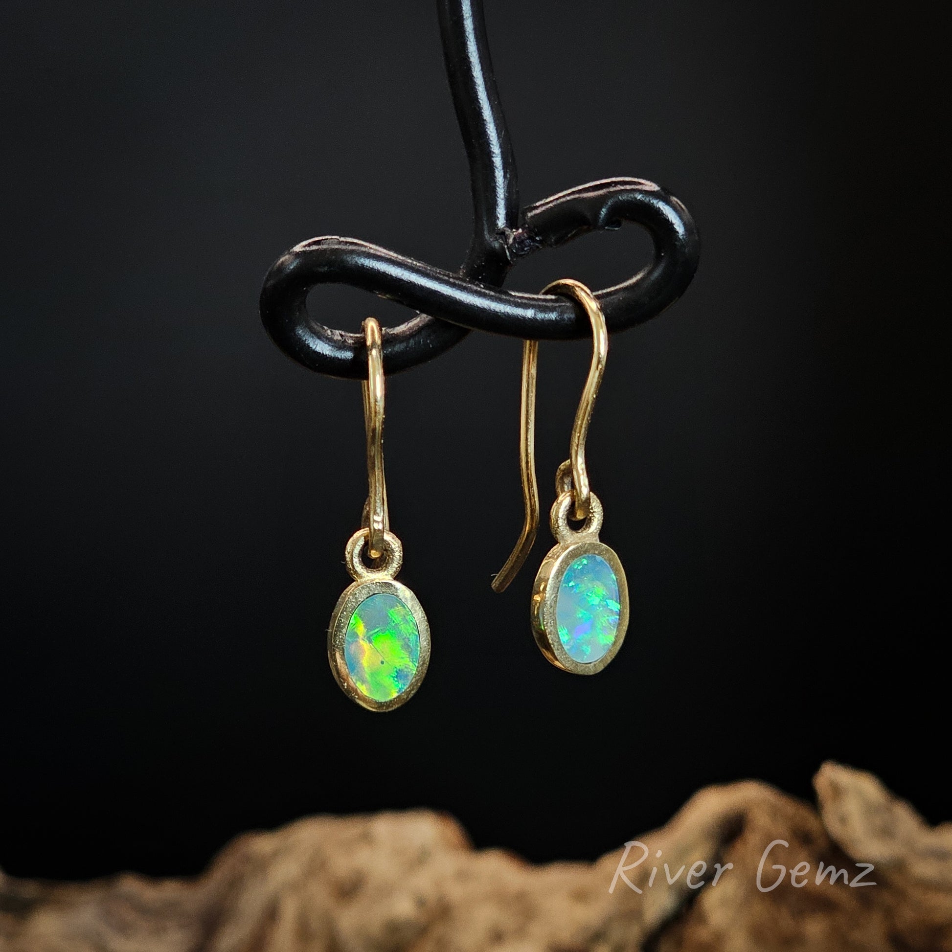Opal earrings on a black stand with a dark background.
