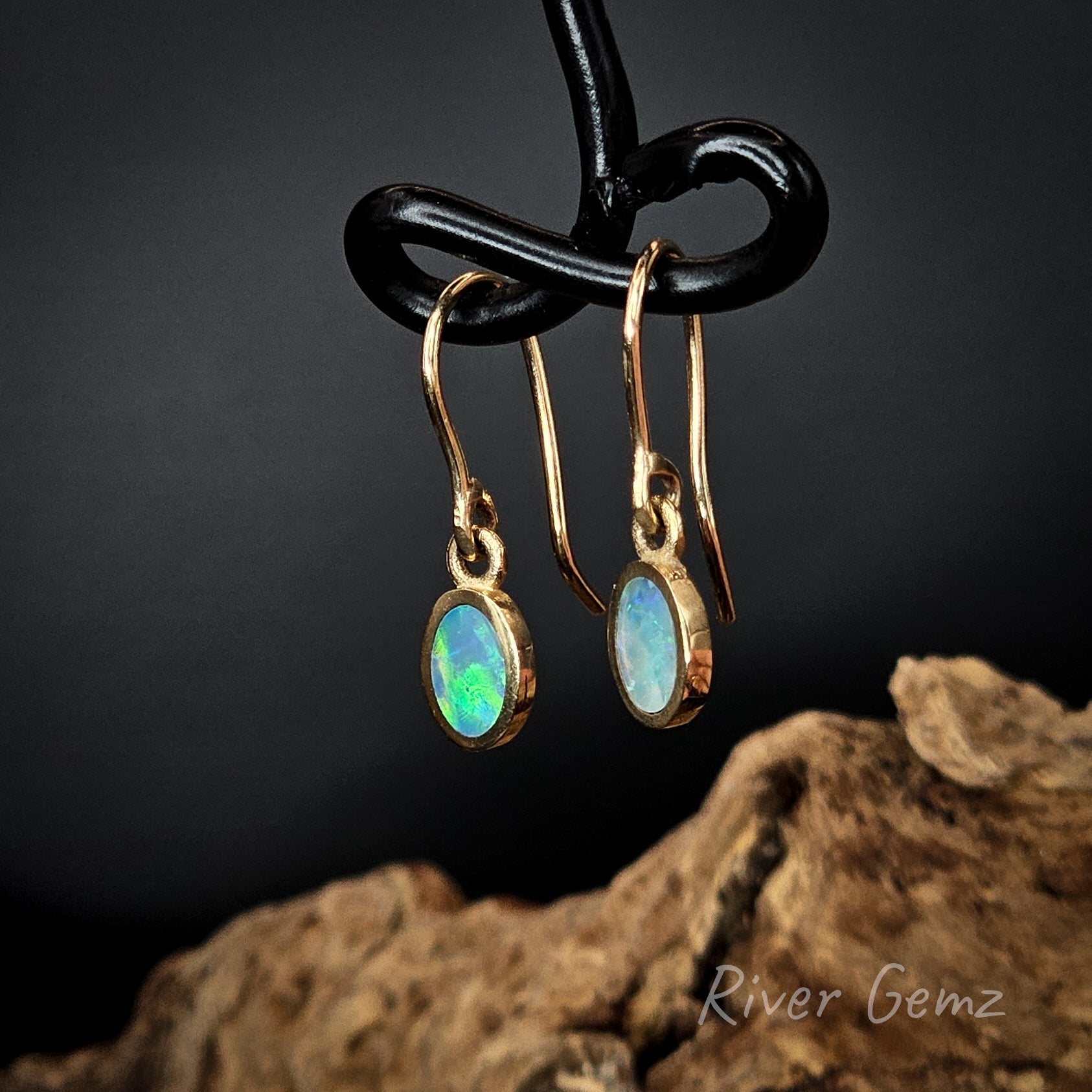 Opal earrings on a black stand with a dark background and 'River Gemz' branding.