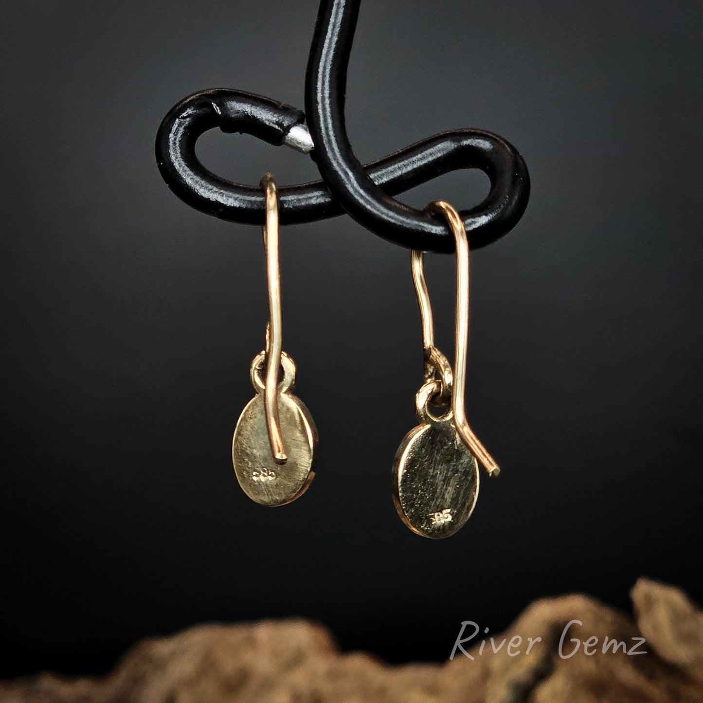 Gold hook earrings on a black wire against a dark background with 'River Gemz' branding.