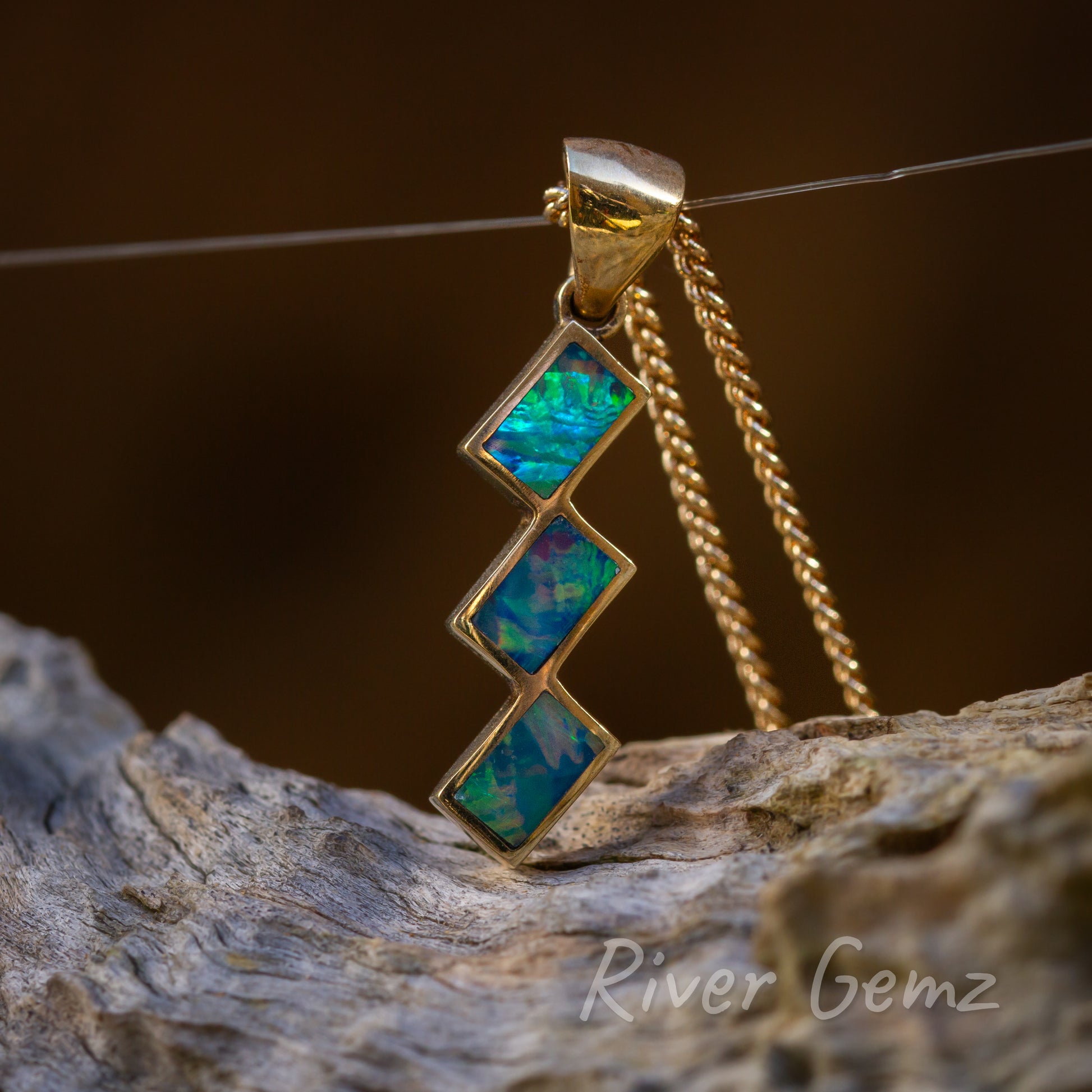 Close up shows the shimmering large spheres of colour in each of the crystal opals. Gold setting stands out from the weathered grey driftwood that the pendant sits above.