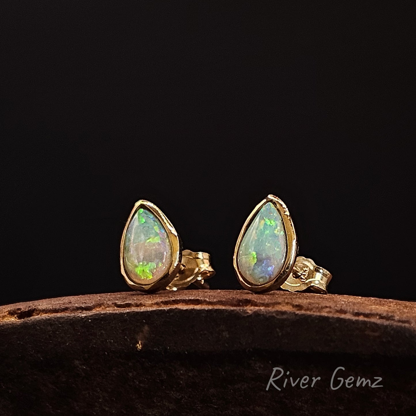 Opal earrings with gold settings on a dark background, branded 'River Gemz'.
