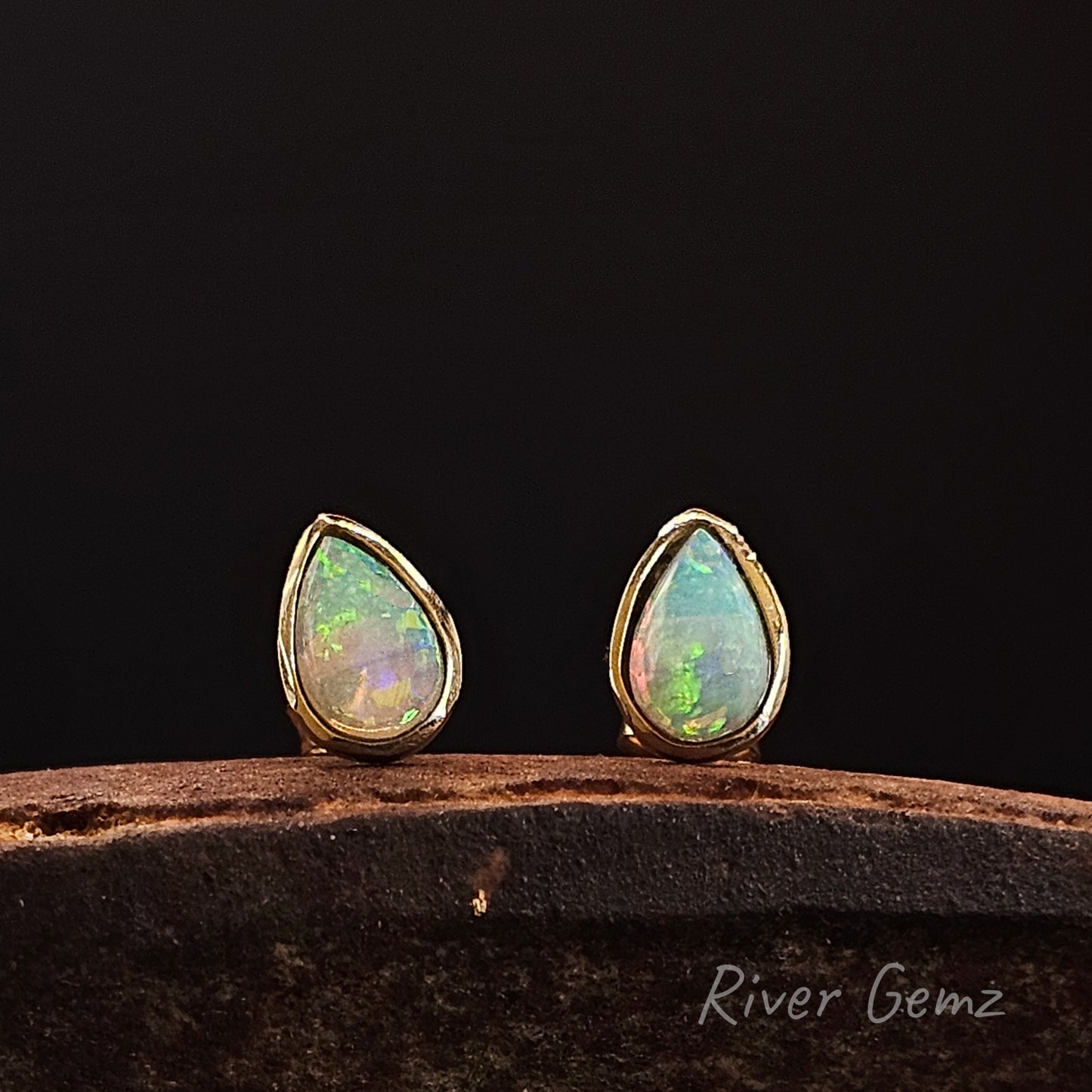 Teardrop-shaped opal earrings with gold settings on a dark background, branded 'River Gemz'.