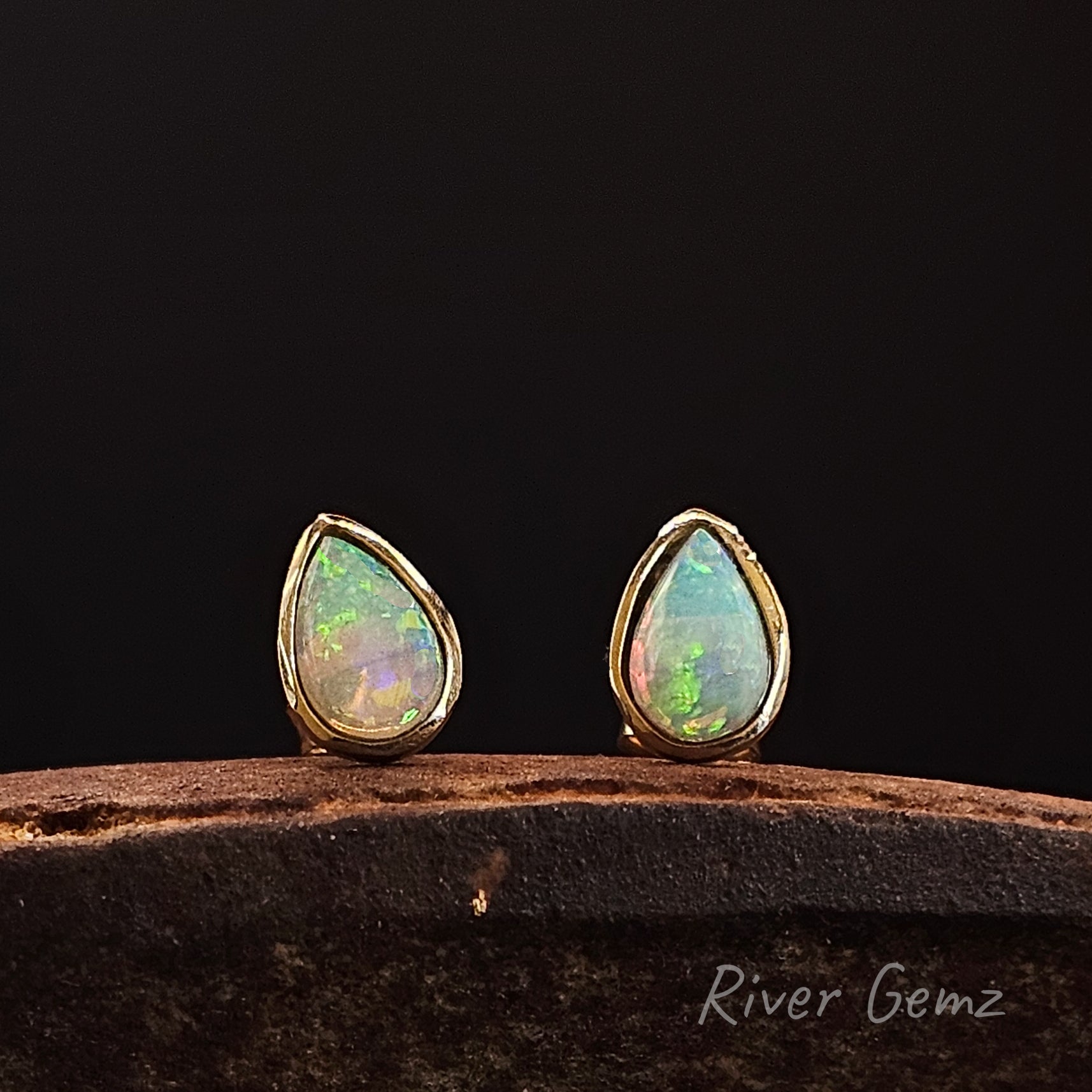 Teardrop-shaped opal earrings with gold settings on a dark background, branded 'River Gemz'.