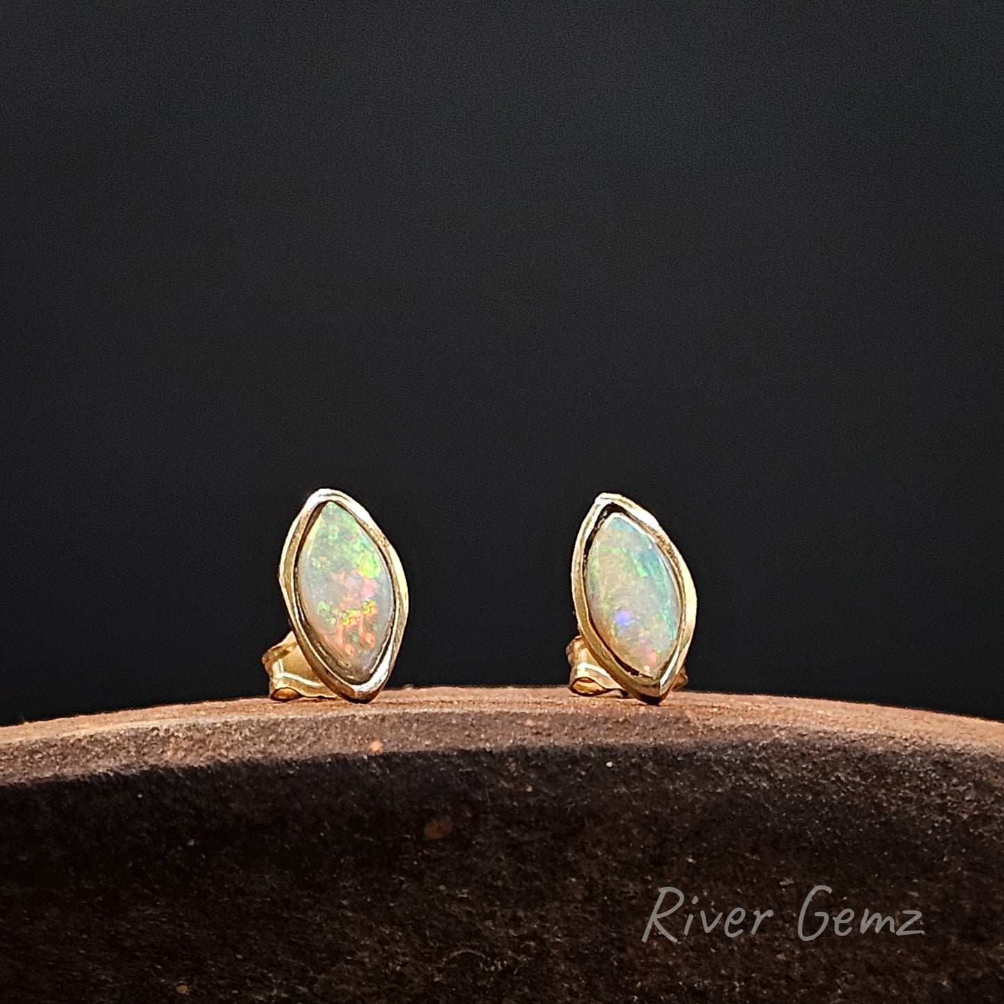 Pair of gold opal earrings on a dark background with 'River Gemz' branding.