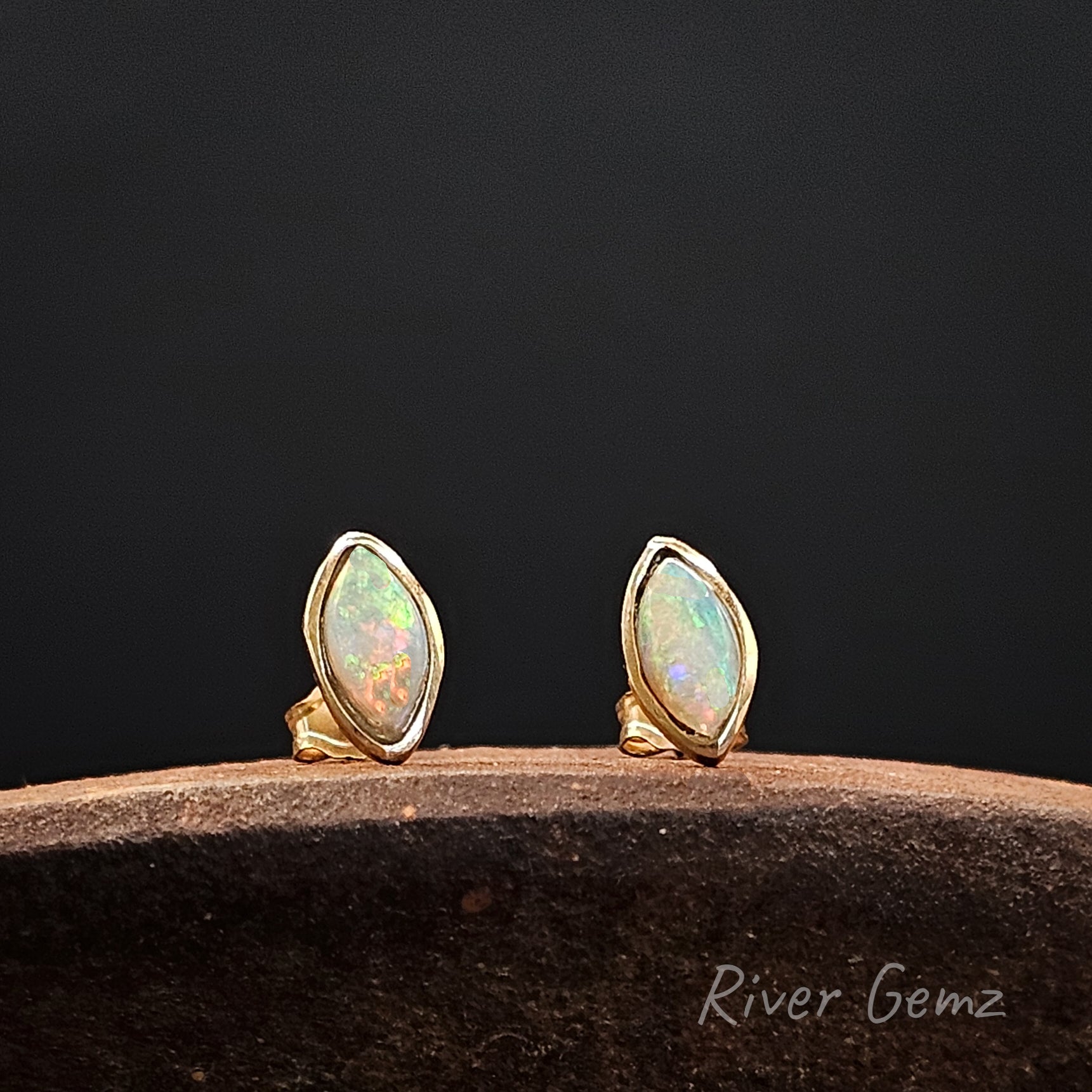 Pair of gold opal earrings on a dark background with 'River Gemz' branding.