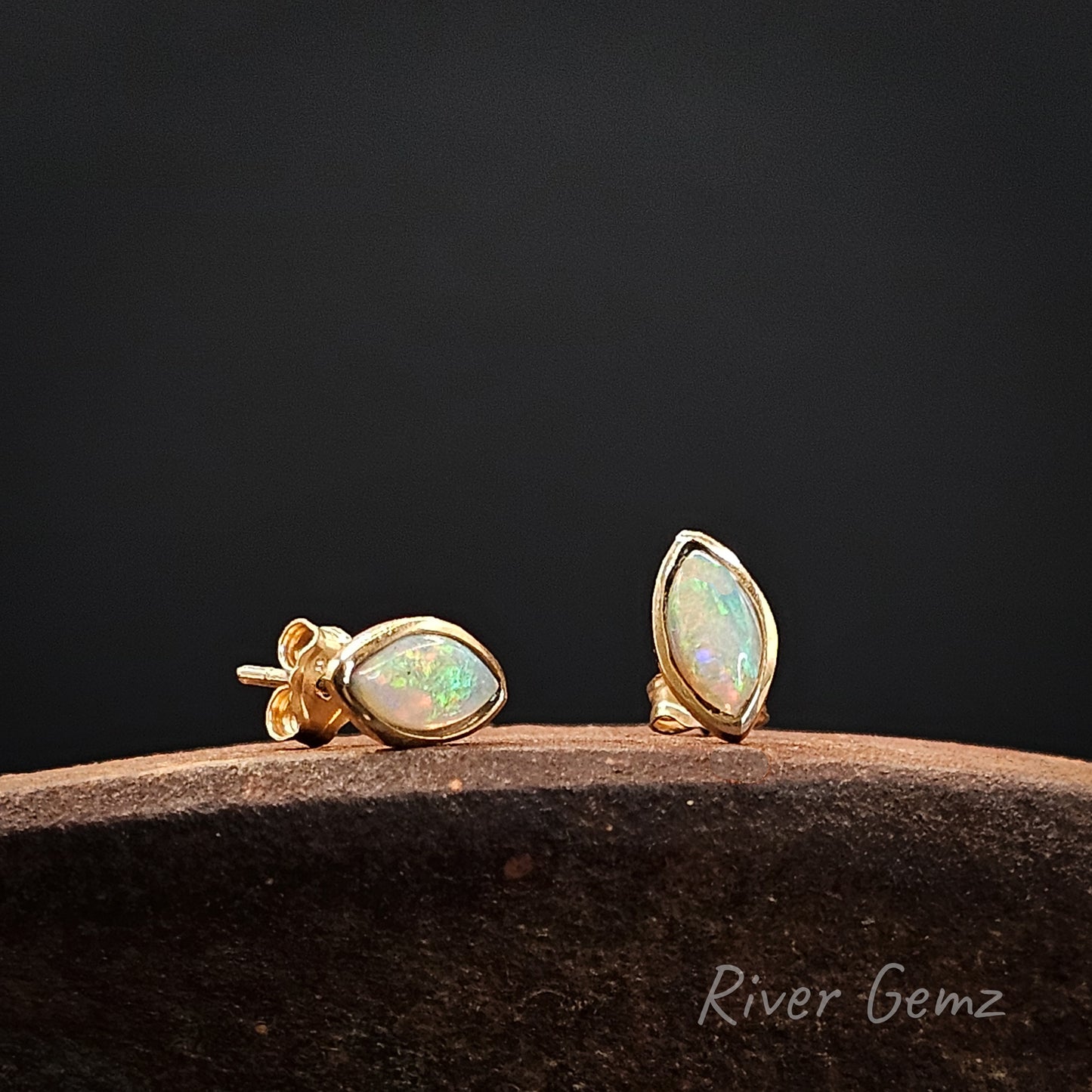 Gold earrings with opal stones on a dark background, branded 'River Gemz'.