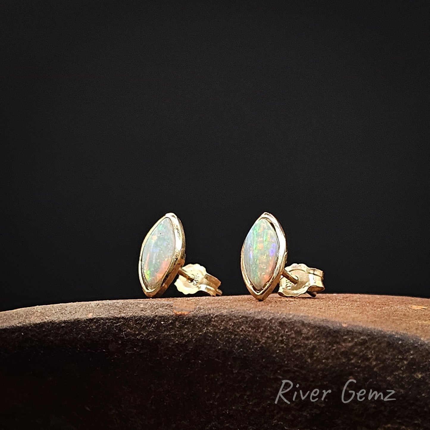 Pair of gold opal stud earrings on a dark background with 'River Gemz' branding.