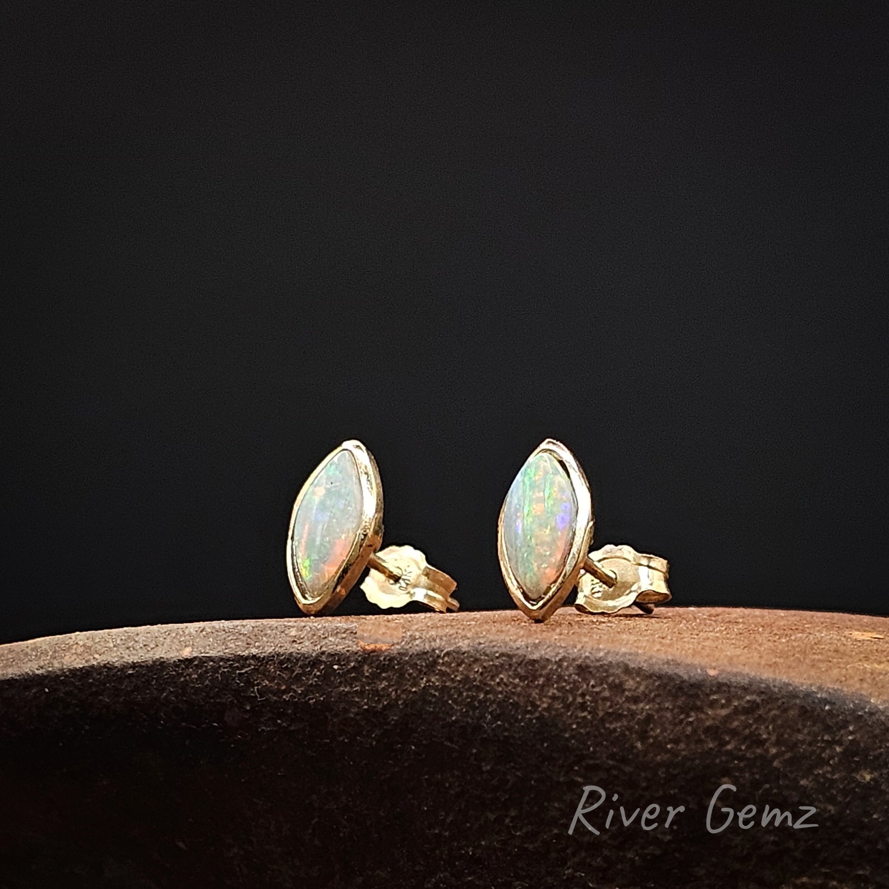 Pair of gold opal stud earrings on a dark background with 'River Gemz' branding.