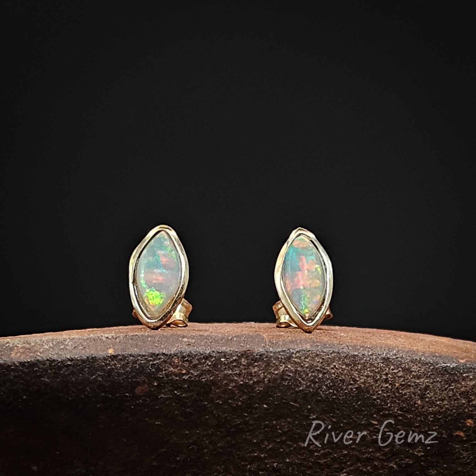 Multi-coloured crystal opals in yellow gold studs on a dark background with 'River Gemz' branding.