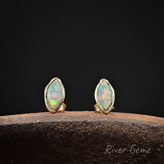Multi-coloured crystal opals in yellow gold studs on a dark background with 'River Gemz' branding.