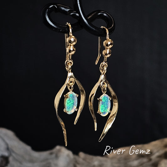 Gold shepherd hook earrings with green crystal opals on a dark background, featuring the brand 'River Gemz'.